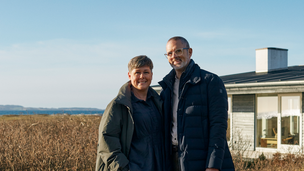 Billede af et par foran et sommerhus ved vandet